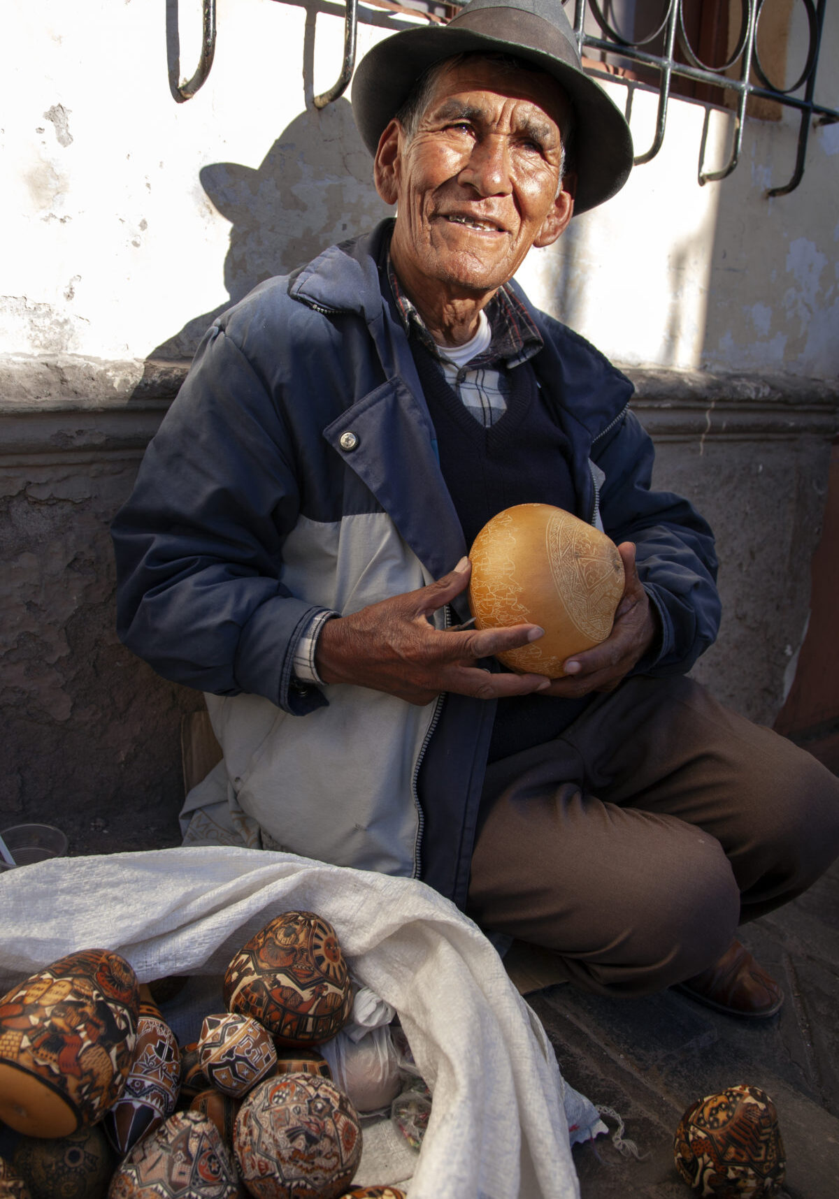 A resident of Cusco, Peru, sits on the sidewalk while carving intricate designs on gourds.